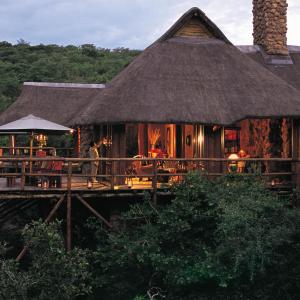 una casa con techo de paja, mesas y sillas en Makweti Safari Lodge en Welgevonden Game Reserve