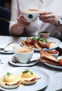 a table with plates of food and a person holding a cup of coffee at Le Monde Hotel in Edinburgh
