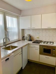 a kitchen with white cabinets and a sink and a stove at Appartement aan het strand De Zeemeermin in Zoutelande +30 photos
