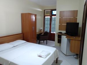 a bedroom with a bed and a desk with a television at Pousada Cavaleiros in Macaé