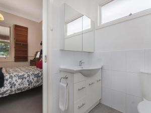 a white bathroom with a sink and a bed at Railway Cottage in Port Fairy