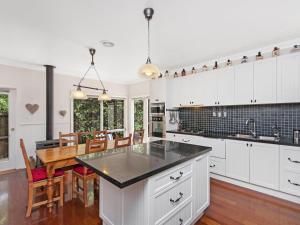 a kitchen with white cabinets and a dining room with a table at Railway Cottage in Port Fairy