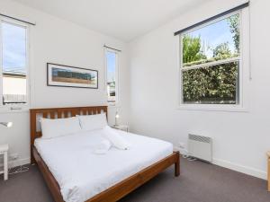 a white bedroom with a bed and two windows at The Church in Port Fairy
