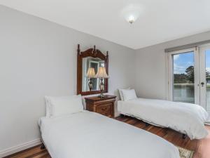 a white bedroom with two beds and a mirror at The Moorings in Port Fairy