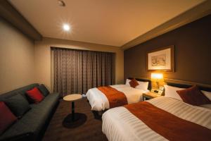 松山市にある道後温泉　ホテルパティオ・ドウゴのベッド2台とソファが備わるホテルルームです。
