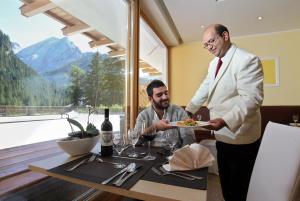 Um homem de fato branco a segurar um prato de comida. em My Kosher Hotel em Canazei