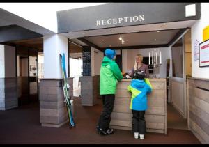 a man and a child standing at a counter in a ski resort at Langley Hôtel Le Petit Prince in L'Alpe-d'Huez