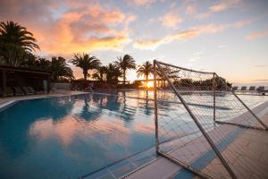 a pool with a volleyball net in front of a sunset at ROBINSON ESQUINZO PLAYA - All Inclusive in Morro del Jable