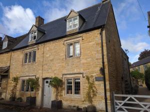 ein altes Backsteinhaus mit schwarzem Dach in der Unterkunft Church Cottage Barn in Longborough