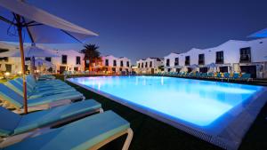 a large swimming pool with chairs and umbrellas at night at FBC Fortuny Resort - Adults Only in Maspalomas