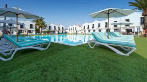 two lounge chairs and umbrellas next to a swimming pool at FBC Fortuny Resort - Adults Only in Maspalomas