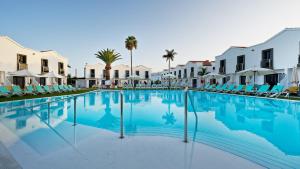 a large swimming pool with chairs and palm trees at FBC Fortuny Resort - Adults Only in Maspalomas