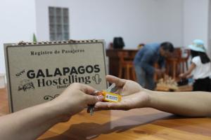 una persona sosteniendo un par de tijeras delante de un cartel en New Galapagos Hostelling, en Puerto Ayora