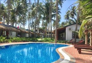 a swimming pool in front of a house with palm trees at The Legend Coco Beach in Mui Ne