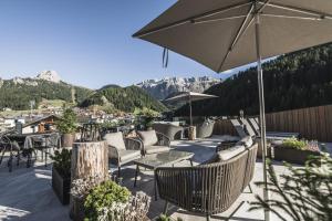 un patio con sillas, mesas y una sombrilla en Hotel Chalet S - Dolomites Design - adults recommended, en Selva di Val Gardena