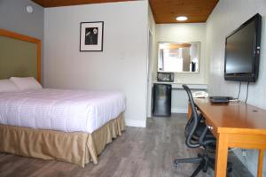 Habitación de hotel con cama, escritorio y TV. en Fraser Inn en Prince George