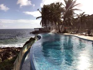 a swimming pool next to the ocean with palm trees at Mercure Salvador Rio Vermelho in Salvador