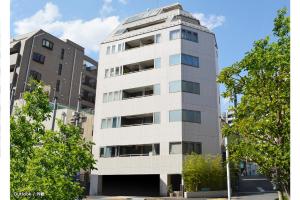 a tall white building with trees in front of it at Guest House Tokyo Azabu in Tokyo