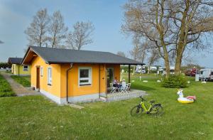 a small yellow house with people sitting in a yard at Knaus Camping- und Ferienhauspark Rügen in Altenkirchen