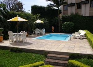 ein Pool mit Stühlen, Tischen und einem Sonnenschirm in der Unterkunft River Hotel in Uruguaiana