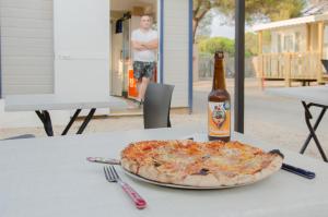 Camping La Bergerie Plage في هييريس: بيتزا جالسة على طاولة مع زجاجة من البيرة