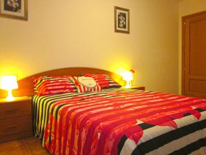 a bedroom with a bed with a striped comforter and two lamps at Apartamentos El Hortalán in Mora de Rubielos