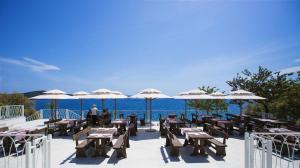 a restaurant with tables and umbrellas and the ocean at Happy Camp mobile homes in Camping Amadria Park Camping Trogir in Seget Vranjica