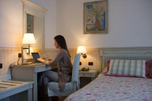 een vrouw aan een bureau met een laptop in een hotelkamer bij Hotel Posta in Moltrasio