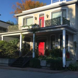 a white house with a red door and stairs at La CAMPAGNE au centre-ville de Baie-Saint-Paul UNIQUE in Baie-Saint-Paul