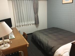 a bedroom with a bed and a desk with a lamp at Garden Hotel Matsumoto in Matsumoto