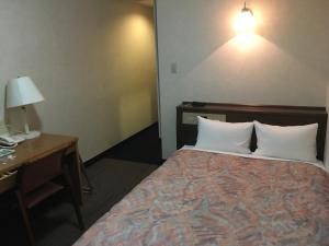 a bedroom with a bed and a desk and a lamp at Garden Hotel Matsumoto in Matsumoto