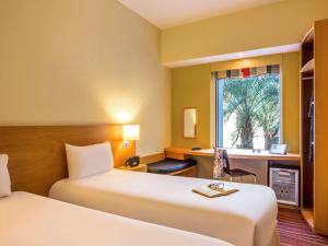 um quarto de hotel com duas camas, uma escrivaninha e uma janela em ibis Mall Avenue Dubai no Dubai