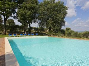 a large swimming pool with blue chairs and trees at Antico Borgo Poggiarello in Monteriggioni