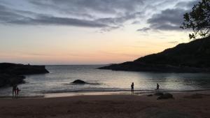 un grupo de personas de pie en la playa al atardecer en Apto Praia de Setiba 2 en Guarapari