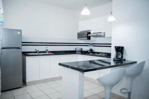 a white kitchen with a black counter and a refrigerator at La Estancia Apartments Mazatlan in Mazatlán