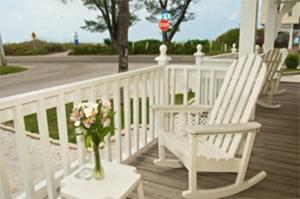 2 weiße Stühle und eine Vase Blumen auf der Veranda in der Unterkunft Queens Gate Resort in Bradenton Beach