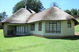 une maison avec un toit de chaume sur une pelouse dans l'établissement Fairways Holiday Accommodation, à Drakensberg Garden