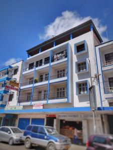 wysoki biały budynek z samochodami zaparkowanymi przed nim w obiekcie Marigold Guest House w mieście Mombasa