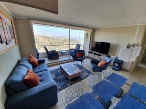 uma sala de estar com sofás azuis e uma grande janela em Algarrobo Laguna Bahia Full em Algarrobo