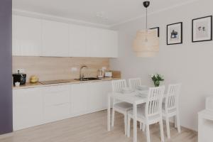 a white kitchen with a white table and chairs at Sosnowe Tarasy in Mielno