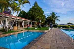 a swimming pool with palm trees and a house at Hotel Brisa do Japi in Cabreúva