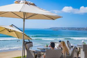 a group of people sitting at a table under an umbrella on the beach at Bay Lodge on the Beach in Mossel Bay