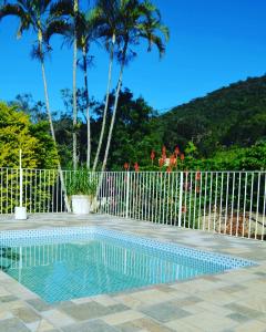 uma piscina em frente a uma cerca com palmeiras em Pousada Primavera da Serra em Serra Negra
