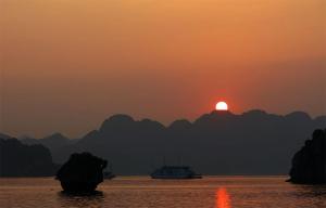 a boat in the water with the sunset in the background at CAT BA VALENTINE Central Hotel in Cat Ba