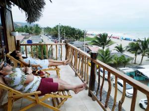 two people sitting in chairs on a balcony looking at the beach at Cocoa Inn Hostal in Canoa