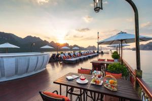 a deck with tables and chairs on the water at sunset at Indochine Cruise Lan Ha Bay Powered by ASTON in Ha Long