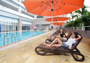 three women sitting in lounge chairs next to a swimming pool at Lexis Suites Penang in Bayan Lepas