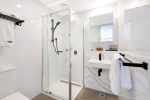 a white bathroom with a shower and a sink at The Hamptons Apartments - St Kilda in Melbourne