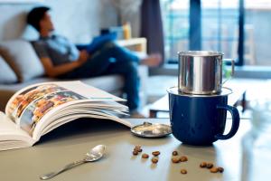 a coffee cup on a table with a book and coffee beans at CIRCADIAN Industrial Loft In Heritage Building in Ho Chi Minh City