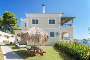 a house with a straw umbrella and a picnic table at Villa iliotropio in Skiathos